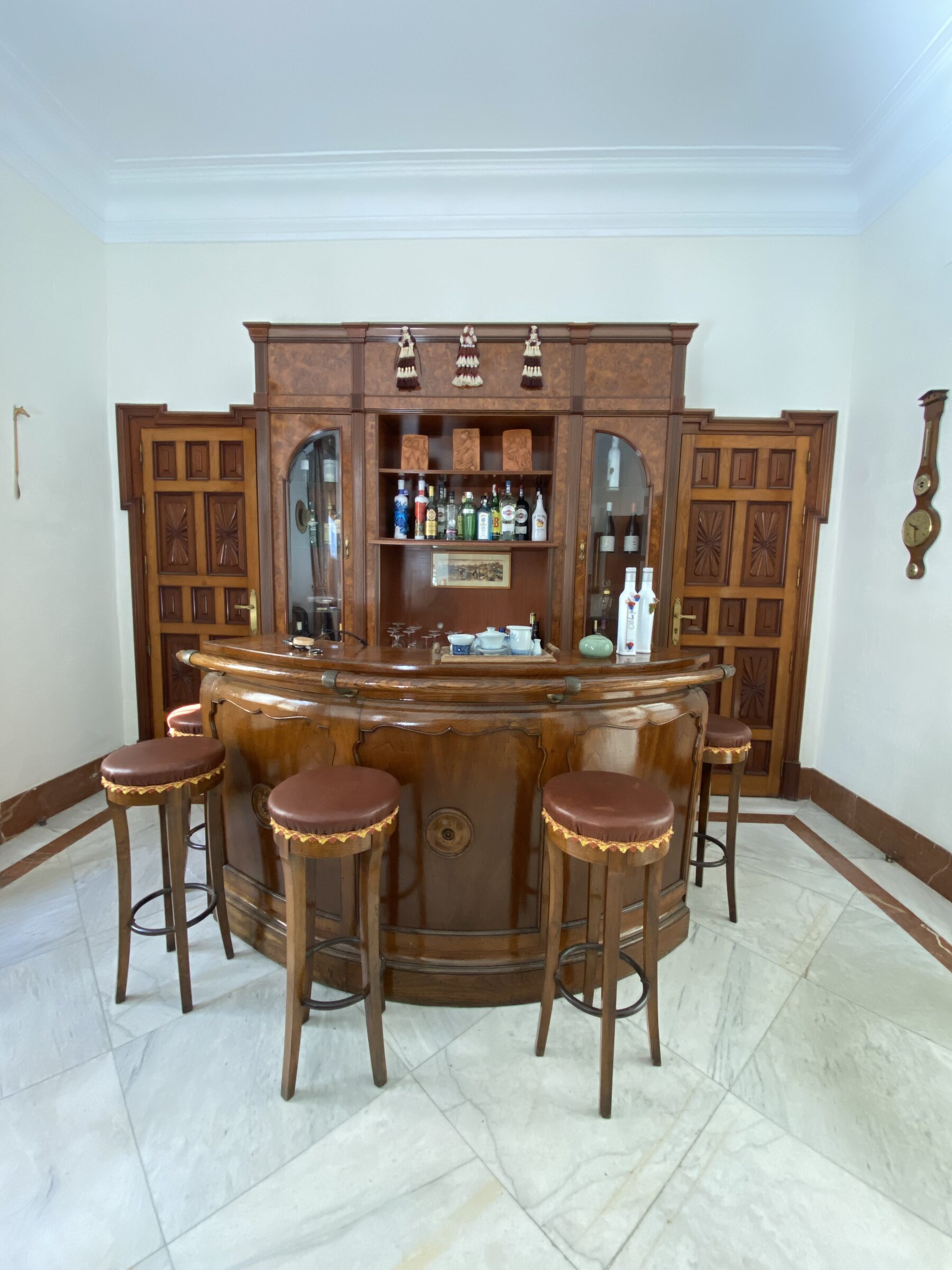 A period burr-wood bar centred between two carved coffered doors, on a marble floor.