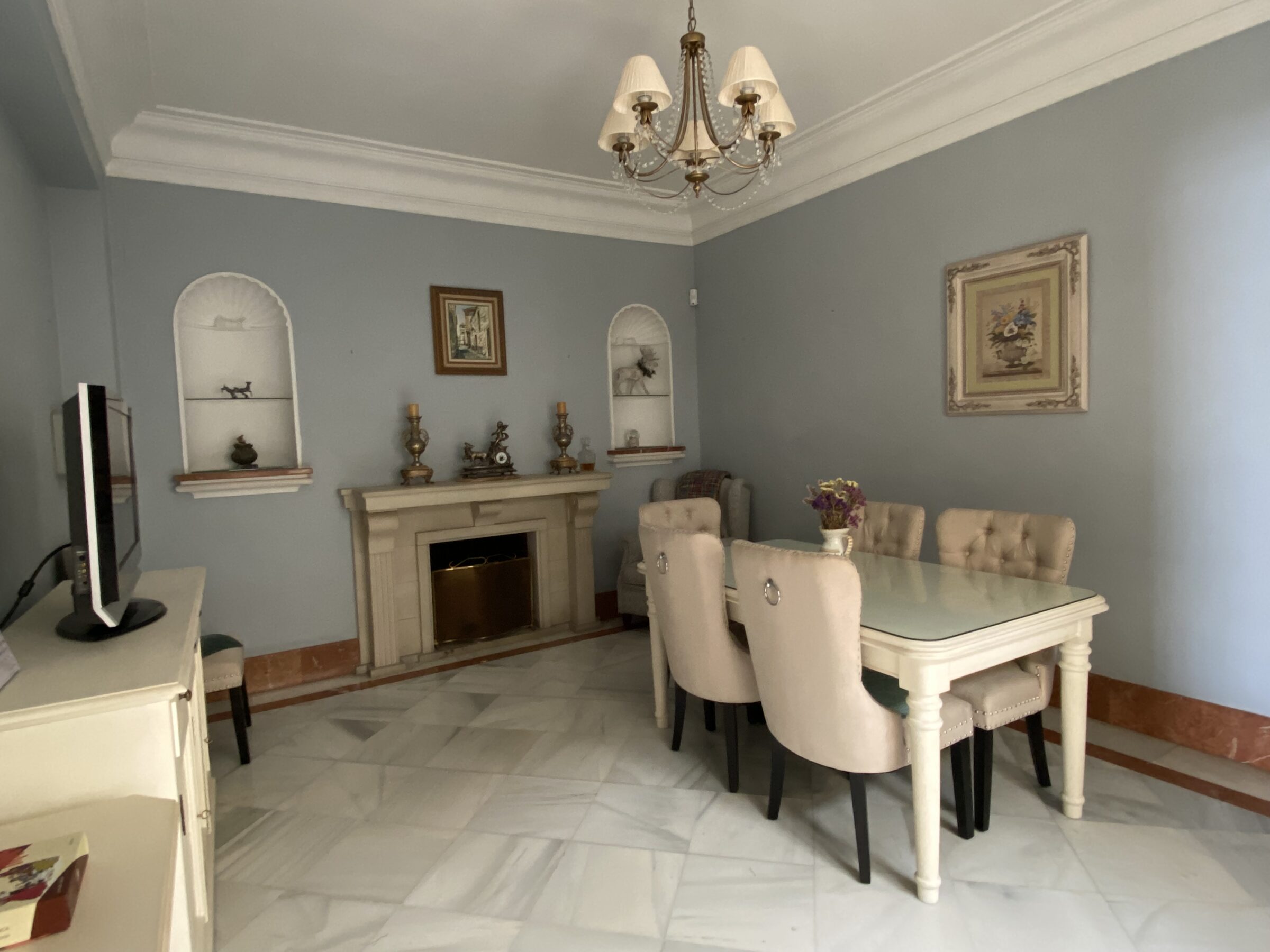 A pale-blue dining room with a stone fireplace, arched niches and a plaster ceiling rosette.