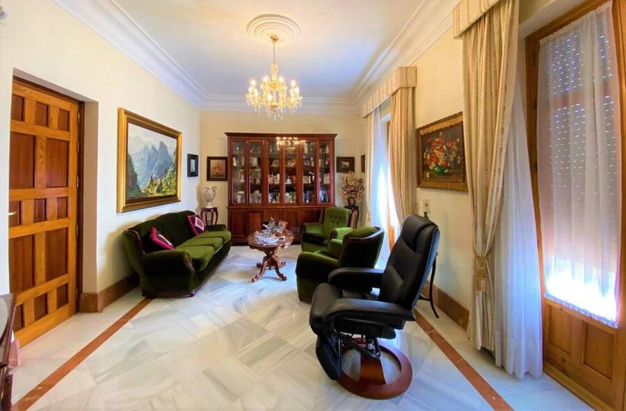 The library: a glass-fronted bookcase against the far wall, two green velvet sofas, a leather chair, and a framed mountain landscape.
