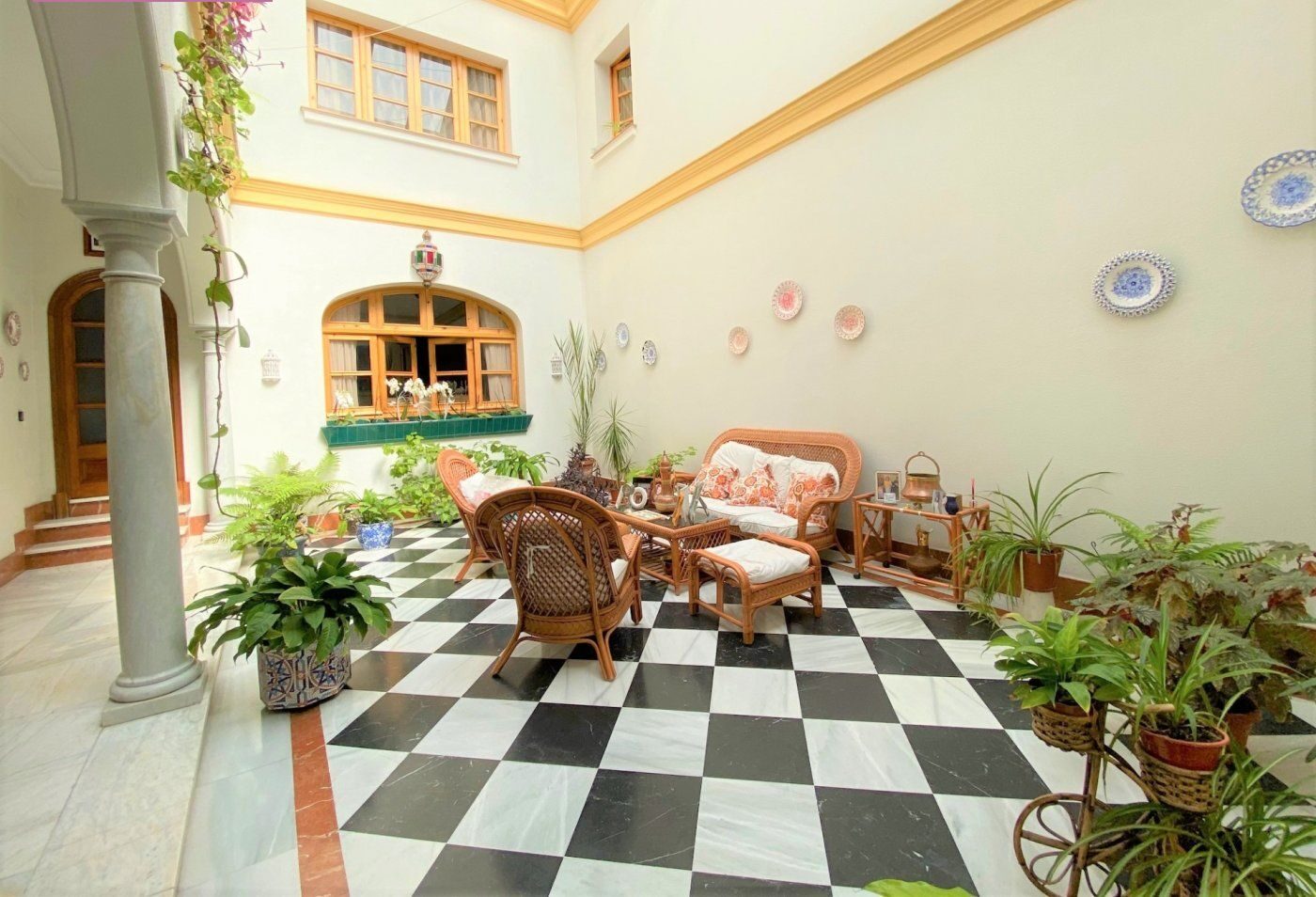 Patio mid-detail — wicker seating set against the black-and-white checkerboard floor, ceramic plates on the wall.